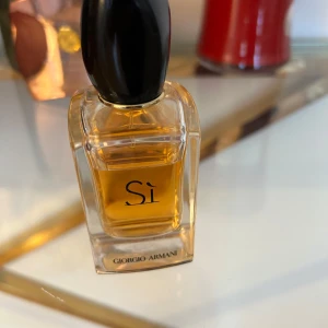 Si från Giorgio Armani - Elegant parfymflaska med en svart kork och gyllene vätska. Flaskan har en stilren design med märkets logga tydligt synlig. Perfekt för den som älskar en sofistikerad doft.