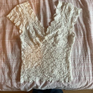 Vit spets linne/topp från Stradivarius - FINNS ÄVEN I SVART! Säljer denna trendiga spetstoppen från Stradivarius. Toppen har en djup v-ringning och korta ärmar och är helt i spets. Perfekt för vardag och fest!💕 Skriv vid frågor!