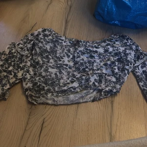 Blommig offshoulder topp - Säljer en söt offshoulder topp med blommigt mönster i blått och beige. Toppen har volangdetaljer och är perfekt för en somrig look. Den är tillverkad i ett lätt och luftigt material.