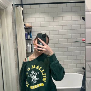 Grön sweatshirt med tryck - Säljer en grön sweatshirt med gult och vitt tryck framtill. Den är använd en gång! Tröjan har en avslappnad passform och långa ärmar. Perfekt för en casual look.