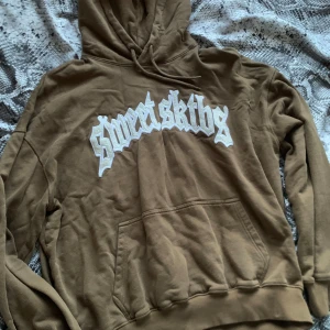 Brun hoodie från Sweet SKTBS - Säljer min bruna hoodie från Sweet SKTBS med skit snygg vit text på framsidan. Den har en klassisk känguruficka och en bekväm huva med dragsko. Perfekt för en avslappnad stil. Är i nyskick😍