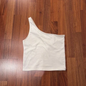Vit ribbad oneshoulder topp - Snygg vit oneshoulder topp med ribbad textur. Perfekt för en stilren och modern look. Passar bra till både jeans och kjol.