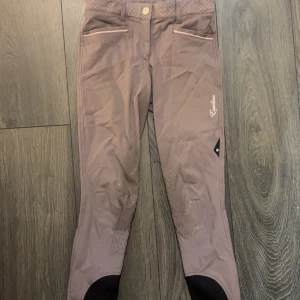 Equiline ridbyxor  - Grå/beige/lila ridbyxor från Equiline, knäskodd med grip. Storlek: Italiensk 38 = Svensk 34. Normalhög midja.  Fint skick, något missfärgade från sadeln men syns knappt (ser värre ut på bilden).  Nypris ca 2700 kr. 