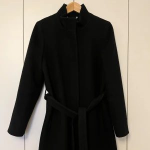 Kappa, Stockh lm, 38, svart - Svart kappa i ull från Stock LM i storlek 38. Kappan är i mycket fint skick. Kemtvättad nyligen och använd max 2 ggr efter det.                         50% ull, 50% polyester, inre materialet är ac 55% polyester och 45% viskos.                                      Längd ca 95 cm, byst ca 48 cm, midja ca 45 cm, ärmlängd mätt från axeln ca 60 cm. 