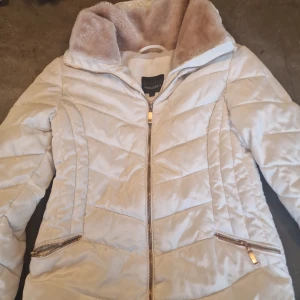 Vit quiltad jacka från Tindra - Säljer en stilren vit quiltad jacka från Tindra med dragkedja och mjukt foder. Jackan har en hög krage och praktiska fickor med dragkedjor. Perfekt för kyliga dagar! Högra fickan sitter dock fast.