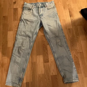 Ljusblå jeans från Weekday - Säljer ett par ljusblå jeans från Weekday med en avslappnad tapered passform. De har klassisk femficksdesign och knappar i midjan. Perfekta för en casual look.