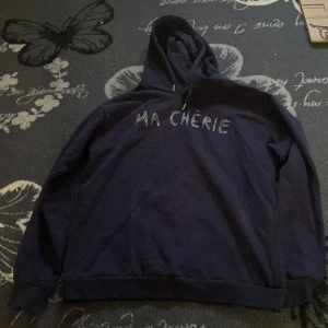 Mörkblå hoodie från Gina Tricot - Säljer en snygg mörkblå hoodie från Gina Tricot med texten 'MA CHÉRIE' i glittriga stenar på bröstet. Den har en klassisk huva med dragsko och långa ärmar. Perfekt för en avslappnad stil. Använd ett fåtal gånger men den är som ny💕