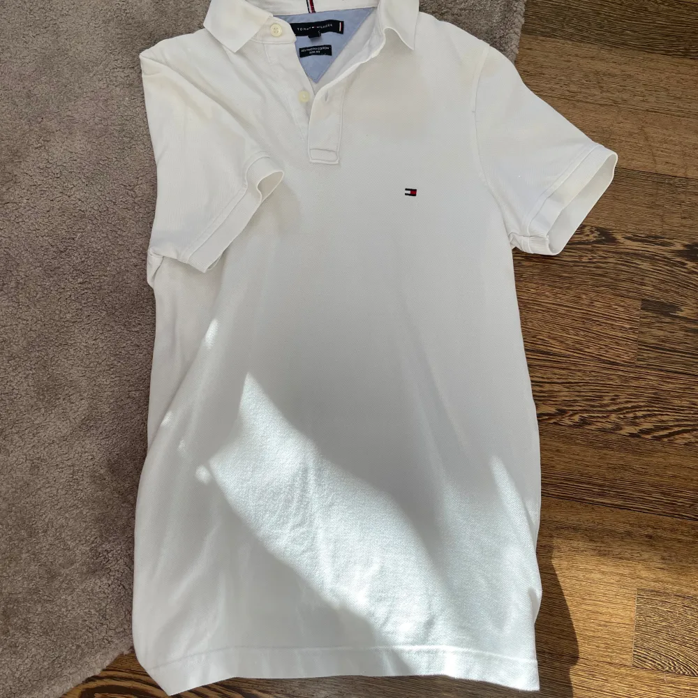 Säljer en stilren vit pikétröja från Tommy Hilfiger i storlek XS. Tröjan har korta ärmar och en klassisk krage med knappar. Den är tillverkad i bomull och har en liten logotyp på bröstet. Perfekt för en avslappnad och snygg look.. Neuletakit & Villapaidat.