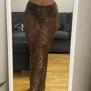 Leopardmönstrad långkjol - Snygg leopardmönstrad långkjol i ett stretchigt mesh material. Kjolen har en tight passform som framhäver figuren och är perfekt för en djärv look. Den är glittrig och ganska genomskinlig, Den är lätt och bekväm att bära. Vet inte midjemmått men den ǎr elastisk. Köpt i asos