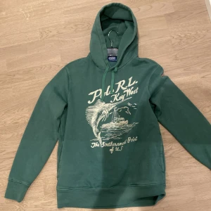 Polo Ralph Lauren key west grön hoodie - Säljer en grön hoodie från Polo RL med tryck av en fisk och texten 'Key West' på framsidan. Storlek M. Den är som helt ny, använd två gånger. Aldrig tvättad. Slutsåld nästan överallt. Priset är diskutabelt vid snabb affär!