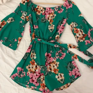 Grön blommig med bälte - Säljer en färgglad grön klänning (byxform nertill) med blommigt mönster. Trekvartsärmar och ett matchande bälte i midjan. Perfekt för sommarens alla tillfällen! 🌸