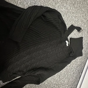 Svart stickad tröja från Ilkbahar Triko - Säljer en svart stickad tröja från Ilkbahar Triko. Tröjan har ett snyggt flätmönster och en hög krage som håller dig varm. Perfekt för kyliga dagar!