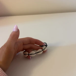 Armband med snäckor - Säljer ett snyggt armband med vita snäckor och svart snörning. Dock så har knytningen gått sönder lite, men de går nog enkelt att fixa💗