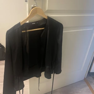 Svart blus - Snygg svart blus från Bik Bok. Den har en elegant design med knytband framtill och långa ärmar. Perfekt för en stilren look.