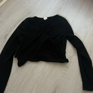 Svart omlottopp från Shein - Säljer en stilren svart omlottopp från Shein. Toppen har långa ärmar och en v-ringad design som ger en elegant look. Perfekt för att matcha med olika outfits.