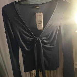 Mörkblå långärmad topp från ginatricot  - Snygg mörkblå långärmad topp med knytning framtill. Perfekt för en stilren look. Toppen har en v-ringad design och är tillverkad i ett mjukt material.