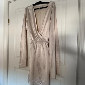 Champagnefärgad omlottklänning - Elegant champagnefärgad omlottklänning med lång ärm och v-ringning.