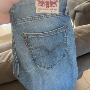 Blå jeans från Levis - Snygga blå jeans från Levis med klassisk femficksdesign och knappgylf. Tillverkade i en bomullsblandning med lite stretch för extra komfort. Perfekta för en avslappnad stil. Rak modell. 