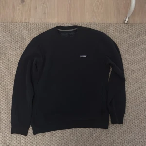 Mörkblå tröja från Patagonia - Säljer en stilren mörkblå tröja från Patagonia. Tröjan har en enkel design med en liten logotyp på bröstet. Perfekt för en avslappnad stil.