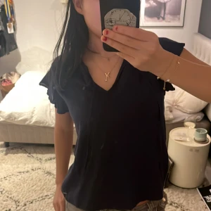 Svart blus med volangdetaljer - Säljer en elegant svart blus med volangdetaljer vid ärmarna. Blusen har en v-ringad design och korta ärmar, perfekt för en stilren look. Passar bra till både jeans och kjol.