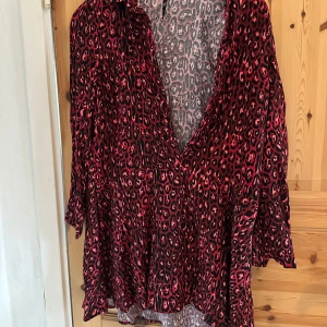 Röd leopardmönstrad tunika från Zara - Snygg röd tunika med leopardmönster från Zara TRF Collection. Tunikan har en v-ringad design och långa ärmar, perfekt för en trendig look.