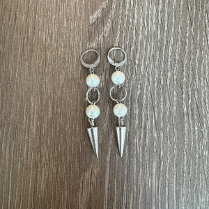 Silvriga örhängen med pärlor  - Snygga örhängen med två vita pärlor i silverfärg. Dem är handgjorde och nickelfria. Perfekta för att ge en edgy touch till din outfit. 