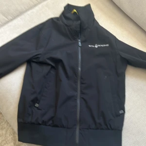 Svart jacka från Sail Racing - Snygg svart jacka från Sail Racing med dragkedja och broderad logga på bröstet. Perfekt för en stilren look. Jackan har en hög krage och ribbade muddar för extra komfort.