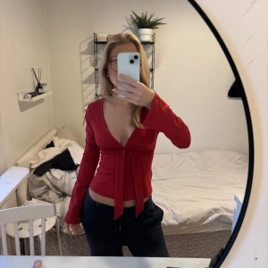Röd v-ringad topp - Snygg röd topp med v-ringning och långa ärmar. Toppen har en knytning baktill som ger en fin detalj, kan knytas både fram och bak. Perfekt för att lyfta vilken outfit som helst. Toppen är från Nelly i storlek xs. Aldrig använt. 