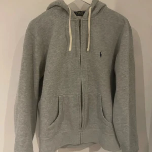 Polo Ralph Lauren hoodie - Säljer en klassisk grå hoodie från Polo Ralph Lauren med drag kedja. Bra sick inga skador eller difekter. Storlek m pris går att diskutera