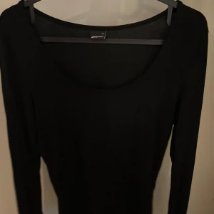 Svart långärmad topp från Gina Tricot - Säljer en stilren svart långärmad tröja med slits på ärmarna från Gina Tricot. Perfekt för en minimalistisk look. Toppen har en rund halsringning och är tillverkad i ett mjukt material.