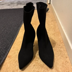 Svarta boots med transparent klack - Snygga svarta boots med spetsig tå och en unik transparent klack. Skorna är stickade och har en tight passform som ger en elegant look. Perfekta för att ge din outfit en modern touch.