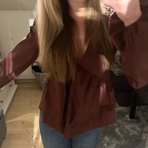 Brun Puffig Blus - Super fin puffig blus med knappar fram, v-uringad och en slit över magen. Köptes för ett tag sedan men har tyvärr aldrig kommit till användning så den är som ny! 