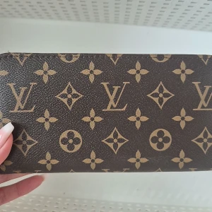 Brun plånbok  - Säljer en elegant brun plånbok med det klassiska monogrammönstret. Plånboken har en stilren design och är perfekt för att hålla dina kort och kontanter organiserade. Ett måste för den stilmedvetna!