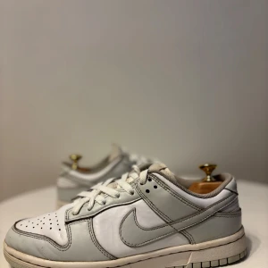 Nike dunk grey fog - Snygga Nike Dunk sneakers i en stilren kombination av vitt och grått. Skorna har klassisk snörning och perforerade detaljer på tån för extra ventilation. Perfekta för en casual look.