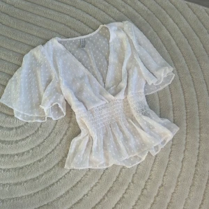 Vit blus från Amisu - Säljer en söt vit blus med prickigt mönster och volangdetaljer. Blusen har en v-ringad design och korta ärmar. Köpt på Plick men passade ej.❤️