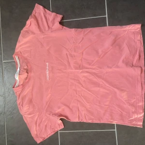 Rosa t-shirt från Calvin Klein Jeans - Säljer en snygg rosa t-shirt från Calvin Klein Jeans. Den har en klassisk passform med korta ärmar och rund hals. Perfekt för en avslappnad stil.