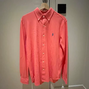 Ralph Lauren skjorta!🍾 - Snygg korallfärgad skjorta från Ralph Lauren med klassisk krage och knappar framtill. Skjortan har en broderad logga på bröstet och är tillverkad i ett lätt och bekvämt material. Priset är inte hugget och skriv vid minsta lilla!👍🏼