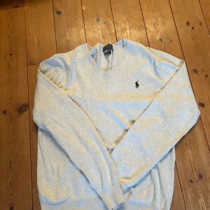 Polo Ralph Lauren Ljusgrå Tröja  - Säljer en stilren ljusgrå tröja från Polo Ralph Lauren i Pima Cotton. Tröjan har en broderad logga på bröstet och en v-ringad hals. Perfekt för en klassisk och avslappnad look.
