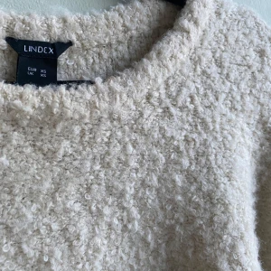 Beige fluffig tröja från Lindex - Mysig beige tröja från Lindex i en fluffig och mjuk textur. Perfekt för kyliga dagar med sin bekväma passform och trekvartsärmar. En stilren och enkel design som passar till många tillfällen.