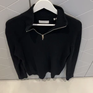 Svart ribbad tröja med dragkedja - Snygg svart ribbad tröja från Jack n Jones med dragkedja vid halsen. Perfekt för en avslappnad look. Tröjan har långa ärmar och en hög krage som kan justeras med dragkedjan.