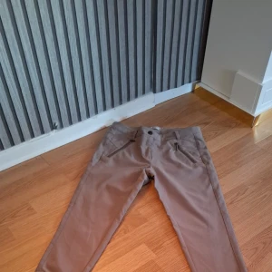 Beige byxor från Fransa - Snygga beige byxor från Fransa med dragkedjor vid fickorna och bensluten. Perfekta för en stilren look. Byxorna har en normal passform och är tillverkade i ett bekvämt material.