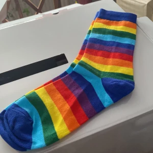 Färgglada randiga strumpor - Säljer ett par färgglada strumpor med regnbågsränder i blått, grönt, gult, orange, rött och lila. Perfekta för att lysa upp vilken outfit som helst! Strumporna är mjuka och bekväma.