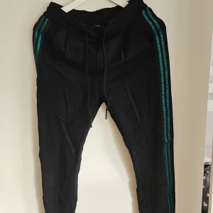 Svarta byxor med turkosa ränder - Snygga svarta byxor med turkosa ränder längs sidorna. Byxorna har en elastisk midja med snörning för justerbar passform. Perfekta för en avslappnad stil.