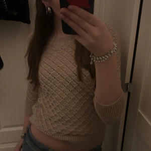 Beige stickad tröja - Säljer en beige stickad tröja med ett snyggt hålmönster. Tröjan har tre kvarts ärmar och ribbade muddar vid ärmslut och nederkant. Perfekt för en stilren och bekväm look.