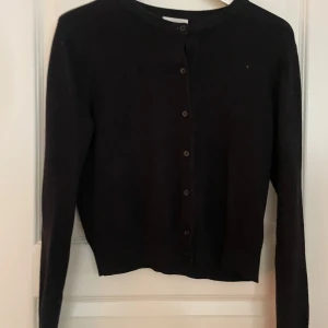 Svart kofta med knappar - Säljer en stilren svart kofta med knappar framtill. Perfekt för lager-på-lager och passar till många olika outfits. Koftan har långa ärmar och en klassisk rund halsringning.