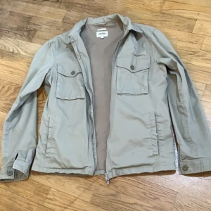 Beige jacka från East West - Säljer en stilren beige jacka från East West. Jackan har dragkedja framtill och två bröstfickor med knappar. Perfekt för en avslappnad look har inte använda den den som ny 