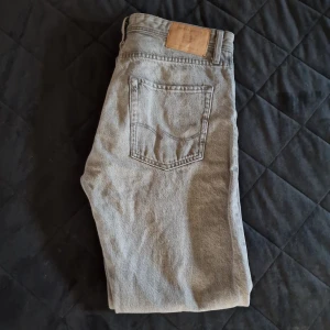 Grå jeansbyxor Relaxed/Chris - Säljer ett par grå jeansbyxor i modellen Relaxed/Chris. De har en avslappnad passform med klassisk femficksdesign och knappgylf. Perfekta för en casual look.