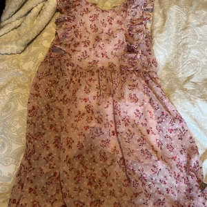 Rosa blommig klänning från Creamie - Söt rosa klänning från Creamie med blommigt mönster och volangdetaljer. Perfekt för somriga dagar med sin luftiga design och charmiga stil. Klänningen har en mjuk och bekväm passform.