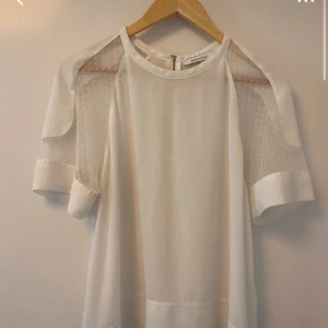 Vit blus från Samsøe Samsøe - Elegant vit blus från Samsøe Samsøe med transparenta detaljer på ärmarna och dragkedja i ryggen. Blusen har korta ärmar och en rund halsringning, perfekt för en stilren look. Storlek S/M