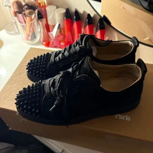 Svarta sneakers med nitar - Säljes: Christian Louboutin [Louis junior spikes flat veau velours] – Storlek [39]   Säljer ett par Christian Louboutin – Storlek 39. Klassiska och eleganta skor med den ikoniska röda sulan, perfekta för både fest och vardag. Finns defekter såsom på sulan, på nitarna men finns extra, och inuti! Alla fem sista bilderna är det sicket jag köpte de från en säljare på Vestiaire Collective. Har kvitton från original köparen. Pm för mer info och bilder!   